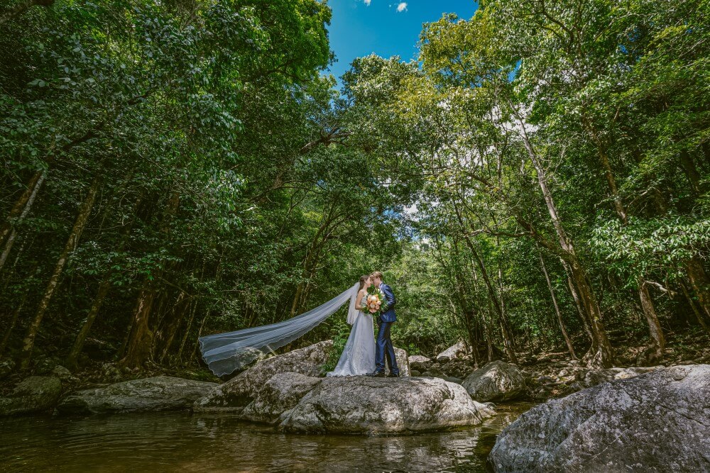bride and groom standing on a big rock in the river