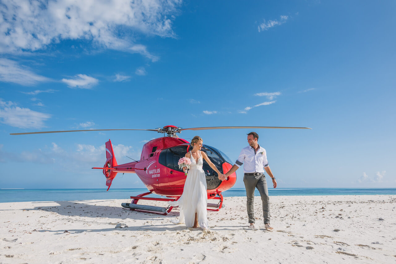 bride and groom standing on beach with helicopter in the background