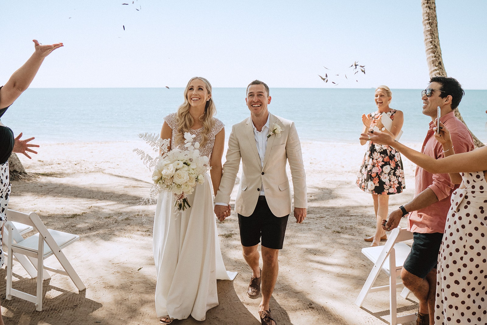 newlywed couple on the beach with guests congratulating them