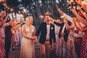 newlywed couple walking down a path with friends holding sparklers above their heads