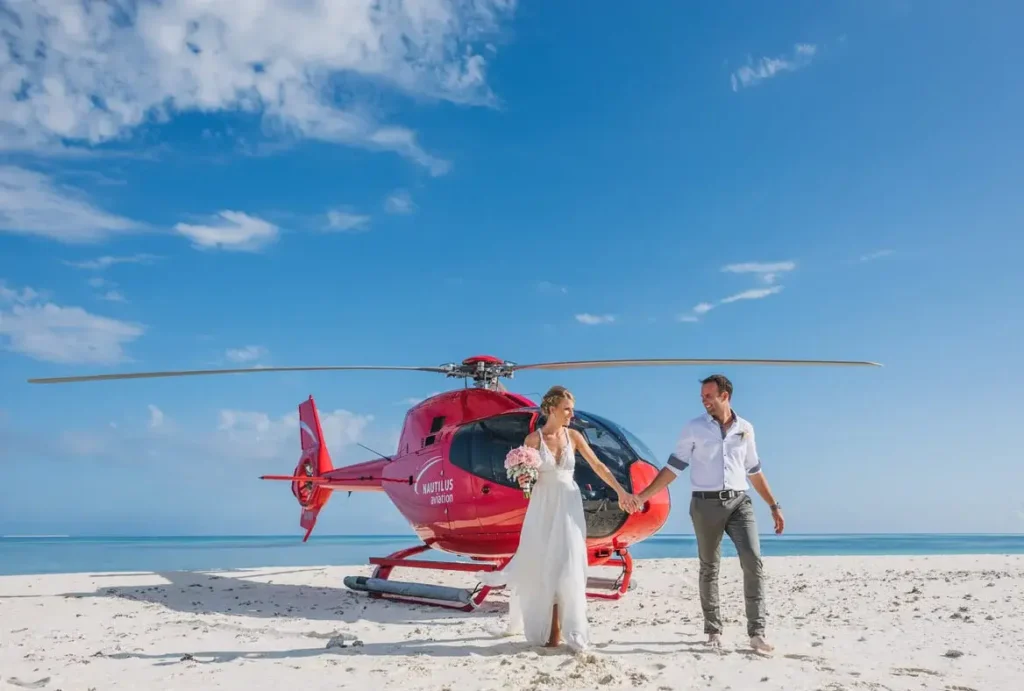 Couple holds hand in front of a red helicopter on a beach