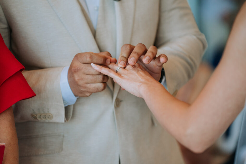 closeup of groom putting a ring on the bride’s ring finger
