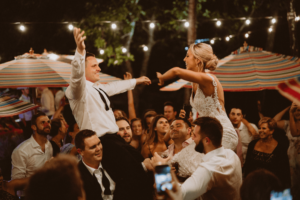 bride and groom lifted up by friends having fun in wedding reception