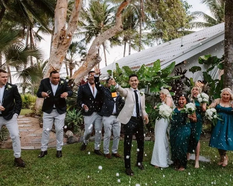 Groom opens a bottle of champagne with the bridal party