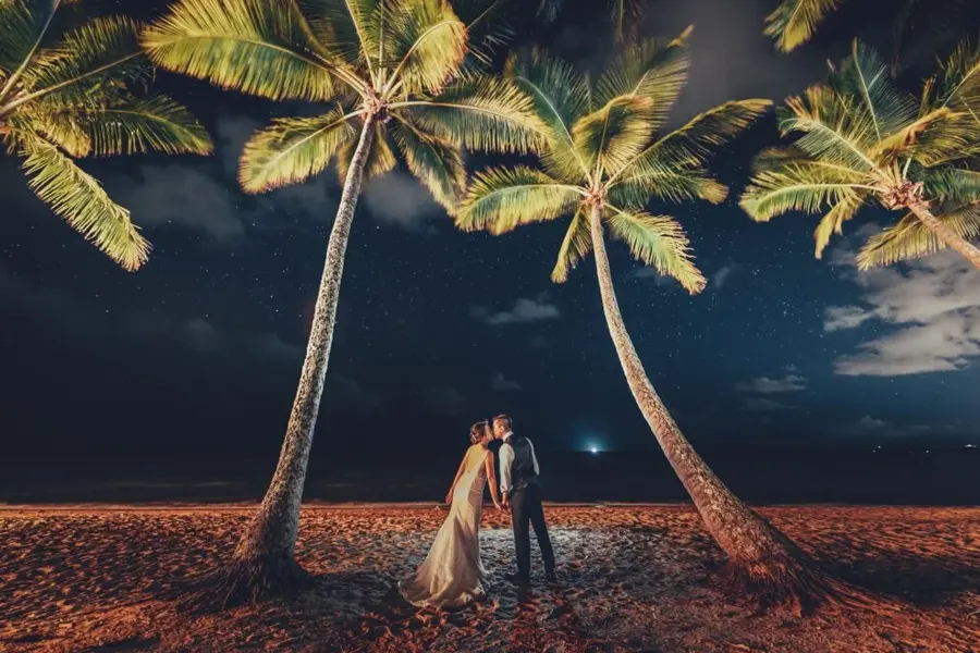 Bride and groom kissing under palm trees and under the moonlight