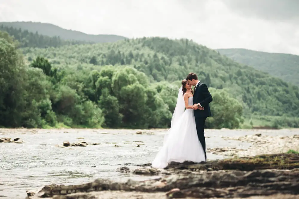 newlyweds kissing and embracing on riverbank
