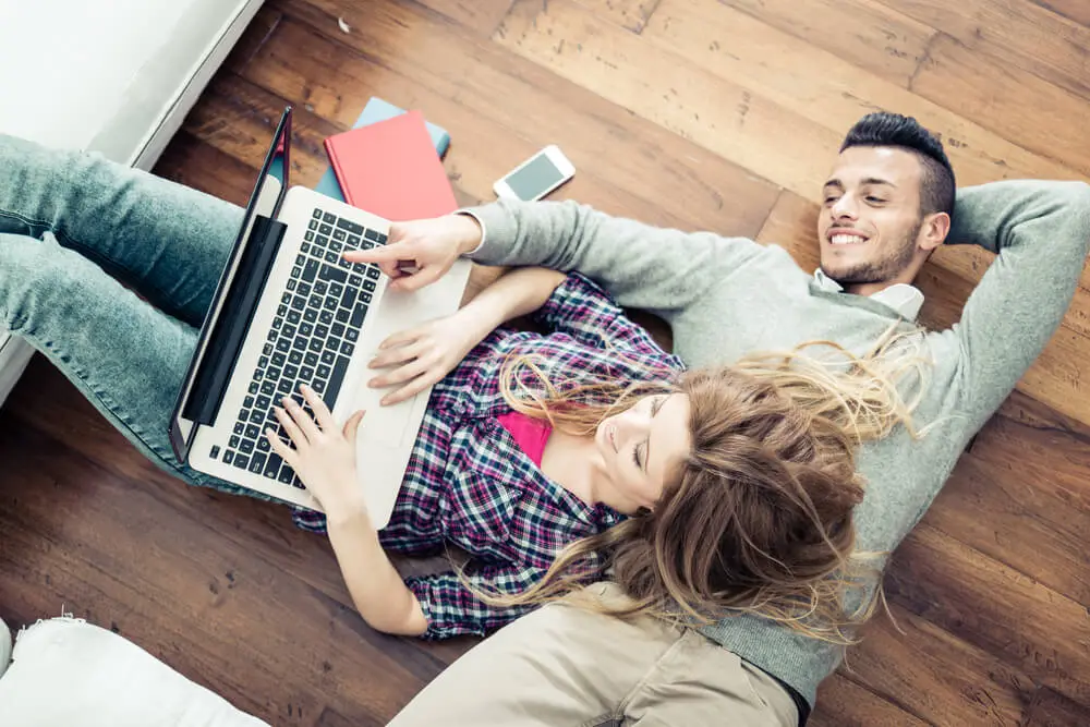 happy couple on the floor browsing on a laptop