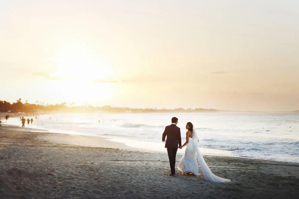 Newlyweds holding hands while strolling along the beach